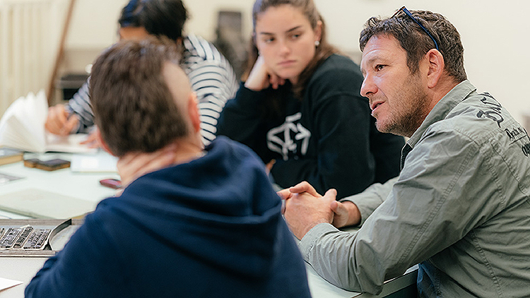 A volunteer sits at a table speaking with several students