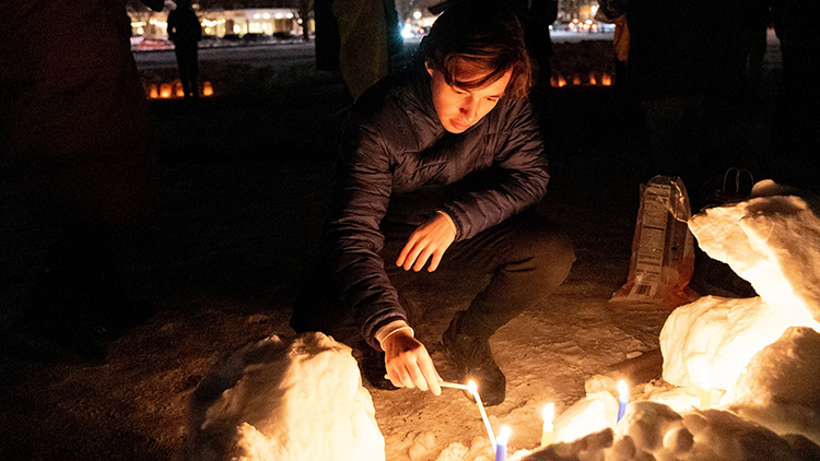 A student bends down by a fire to light a candle on the Green