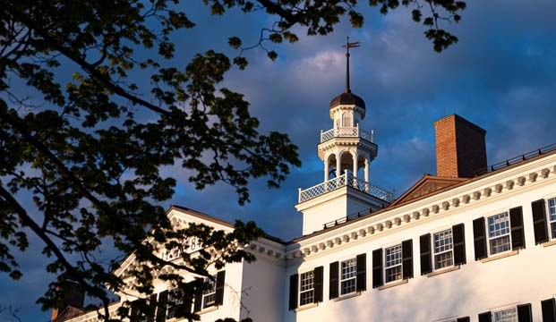 Photo of Dartmouth Hall framed by tree branches against a partly cloudy sky