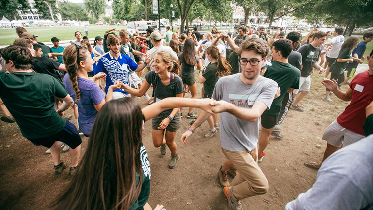 A large group of first years gather on the green with many students holding hands in a circle