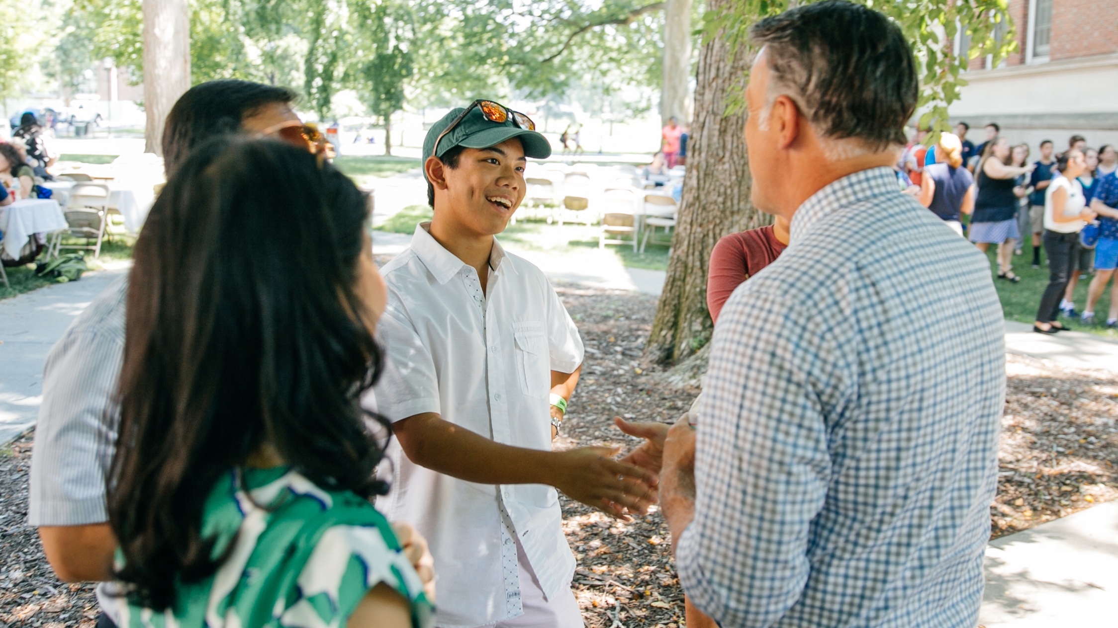 A photo of a male alum shaking hand with a young student outdoors on campus.