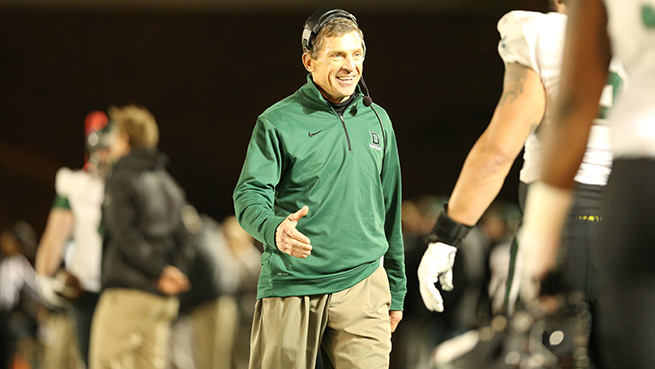 A photo of the late Buddy Teevans on the football field walking toward a student-athlete, smiling, with his hand extended for a hand shake.