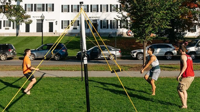 A group of three male students playing volleyball outside on the Green.