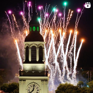 fireworks illuminate the night sky behind a green-lit Baker Bell Tower